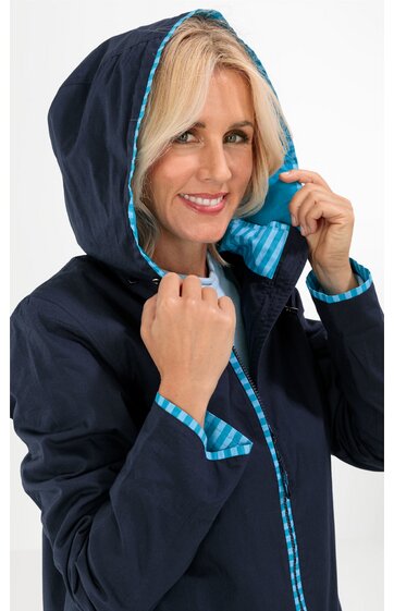 Dunkelblauer Kapuzenmantel mit türkis-weiß gestreiftem Innenfutter an Kapuze und Reißverschluss, lange Ärmel, figurbetonte Form, getragen von stehender Frau, Kapuze anhebend