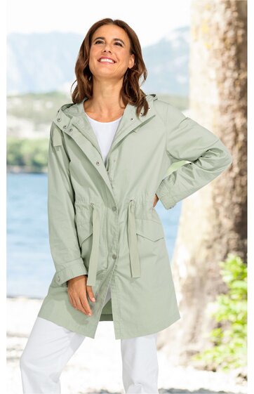Hellgrüne Damenjacke mit Kapuze, Tunnelzug in der Taille, seitlichen Eingrifftaschen, langen Ärmeln, durchgehendem Reißverschluss, getragen von stehender Frau mit linker Hand in der Hüfte, weiße Hose