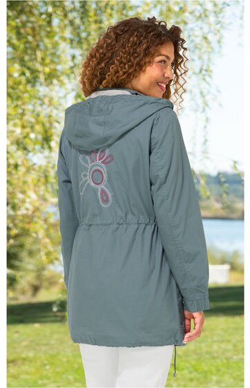 Hellblaue Kapuzenjacke mit Kordelzug, lange Ärmel, Tunnelzug an der Taille, hinten mit floralem pinkem Aufdruck, getragen von seitlich stehender Frau im Freien