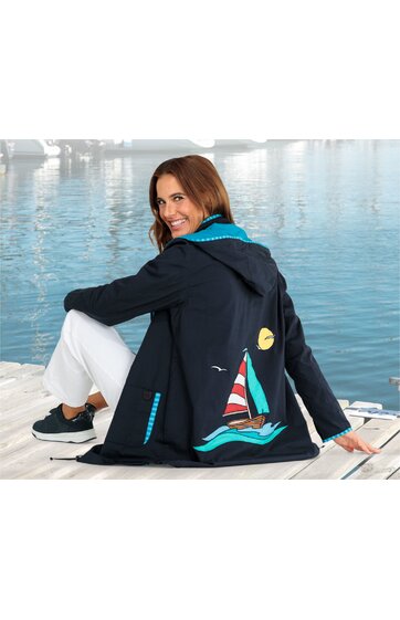 Damenjacke in Dunkelblau mit blau-türkis gestreiftem Innensaum, Segelbootmotiv in Rot, Weiß, Braun und Türkis auf Rückseite mit gelber Sonne und weißer Möwe, Kapuze, seitliche Taschen, getragen von sitzender Frau am Wasser