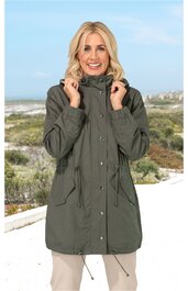 Grüner Parka mit Kapuze, durchgehender Frontreißverschluss und Druckknöpfen, Tunnelzug an Taille und Saum, große aufgesetzte Taschen, getragen von lächelnder stehender Frau vor Strandhintergrund