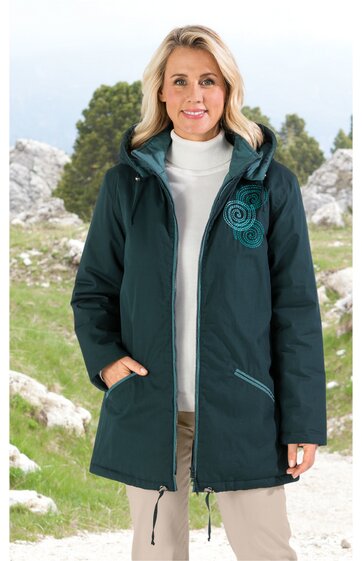 Dunkelgrüne, lange Damenjacke mit Kapuze, grüner spiralförmiger Druck auf der linken Schulter, zwei Reißverschlusstaschen, durchgehender Frontreißverschluss, getragen von stehender Frau mit weißen Haaren, weißer Rollkragenpullover darunter