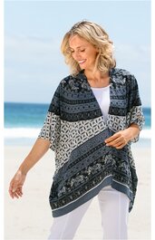 Ponchoartige Bluse in Dunkelblau und Creme mit geometrischem Muster, V-Ausschnitt, halblange Ärmel, asymmetrischer Saum, getragen von lächelnder stehender Frau am Strand, lockere Passform