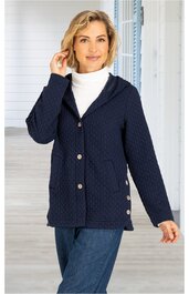Dunkelblaue Strickjacke mit Punktmuster, Knöpfe vorne und an der Seite, Kapuze, lange Ärmel, locker geschnitten, getragen von stehender Frau mit weißem Rollkragenpullover und blauen Jeans