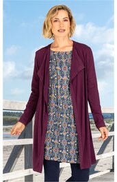 Lila lange offen fallende Jacke, Rückenlänge, lange Ärmel, getragen von stehender Frau, darunter knielanges blaues Kleid mit buntem Blumenmuster, Rundhalsausschnitt