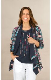 Damen-Set bestehend aus dunkelblauem T-Shirt mit buntem Linienmuster, Rundhalsausschnitt, locker sitzend, bunte Strickjacke mit Muster aus geometrischen Formen und floralen Motiven, offene Vorderseite, weiße Hose, getragen von stehender Frau mit offe