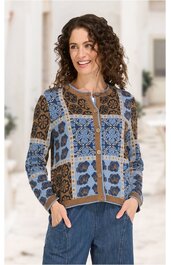 Langärmlige Strickjacke mit blau-braunem Blumen- und Ornamentmuster, Rundhalsausschnitt, Knopfleiste vorne, gerade geschnitten, getragen von lächelnder stehender Frau mit halb offenen Händen in Hosentaschen