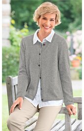 Grau melierte Strickjacke, Knopfleiste, weißes Hemd mit Kragen darunter, getragen von sitzender älterer Frau, beige Hose, entspannte Outdoor-Situation