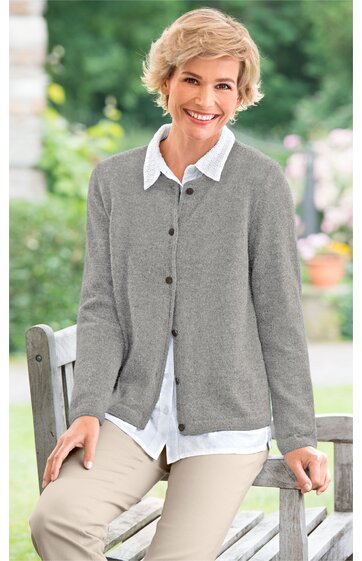 Grau melierte Strickjacke, Knopfleiste, weißes Hemd mit Kragen darunter, getragen von sitzender älterer Frau, beige Hose, entspannte Outdoor-Situation