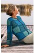 Frau sitzt entspannt auf einem Steg am Wasser, trägt einen blauen Pullover
