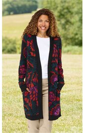 Lange Strickjacke in Dunkelblau mit buntem Blumenmuster, offene Vorderseite, lange Ärmel, zwei Eingrifftaschen, getragen von stehender Frau mit lockerem Haar, weiße Bluse darunter, beige Hose