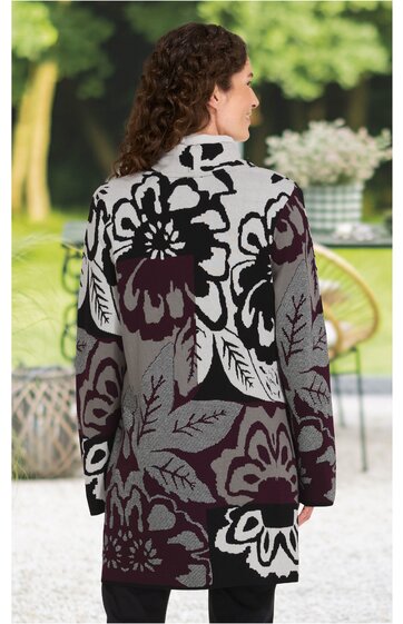 Lang geschnittener Pullover in Grau mit großen floralen Mustern in Schwarz und Dunkelrot, hoher Kragen, lange Ärmel, getragen von stehender Person mit dem Rücken zur Kamera