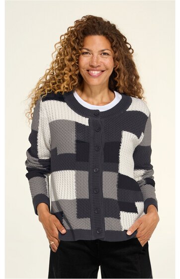 Damenstrickjacke mit Knöpfen, schwarz-weiß-grau kariert, Rundhalsausschnitt, lange Ärmel, gerade geschnitten, getragen von lächelnder stehender Frau mit lockigen Haaren, Hände in Taschen