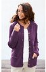 Lila Strickjacke mit langen Ärmeln, Rundhalsausschnitt, durchgehende Knopfleiste mit braunen Knöpfen, zwei aufgesetzte Taschen vorne, gerade geschnitten, getragen von lächelnder Frau mit dunklen Haaren, weiße Bluse und helle Hose darunter