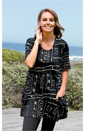 Schwarze Tunika mit weißem geometrischem Muster, kurze Ärmel, Rundhalsausschnitt, lockere Passform mit Bindegürtel in der Taille, getragen von lächelnder Frau im Stehen, mit Hand in Tasche