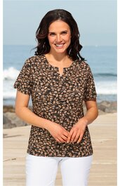 Damenbluse in dunkelbraun mit beigem Blumenmuster, kurze Ärmel, Rundhalsausschnitt mit kleinem V-Schlitz, gerade geschnitten, getragen von lächelnder, stehender Frau am Strand
