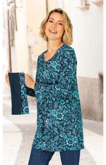 Langarm-Tunika in petrolblau mit hellblauem Blumenmuster, runder Ausschnitt, gerade geschnitten, getragen von stehender lächelnder Frau, mit passendem Muster-Schal in der Hand