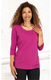 Fuchsiafarbenes Langarmshirt ohne Muster, Rundhalsausschnitt, gerade geschnitten, getragen von stehender Frau mit einer Hand auf der Brust