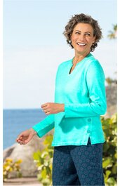 Türkisfarbener Pullover mit V-Ausschnitt, langärmlig, seitliche Schlitze, getragen von lächelnder Frau im Freien, kombiniert mit dunkelblauen, gemusterten Hosen