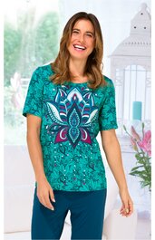 Türkisgrünes T-Shirt mit großem, mehrfarbigem Mandala-Muster in Blau, Weiß und Pink auf der Vorderseite, Rundhalsausschnitt, kurze Ärmel, getragen von lächelnder, stehender Frau, locker sitzend