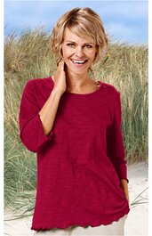 Rotes Langarmshirt, unifarben, rundhals, lockere Passform, gerader Saum, getragen von lächelnder Frau mit kurzem blondem Haar, stehender Pose vor Strandgras