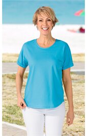 Hellblaues T-Shirt mit Rundhalsausschnitt und kurzen Ärmeln, gerade geschnitten, getragen von stehender lächelnder Frau vor Strandhintergrund