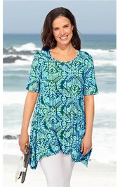 Tunika in Blau- und Grüntönen mit floralem Muster, rundem Halsausschnitt, dreiviertel langen Ärmeln, asymmetrischem Saum, getragen von lächelnder Frau am Strand, locker geschnitten