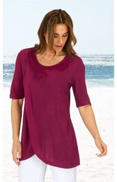 Damenoberteil in dunklem magenta, unifarben, rundhals, halbe Ärmel, asymmetrischer Saum, getragen von stehendem Modell am Strand