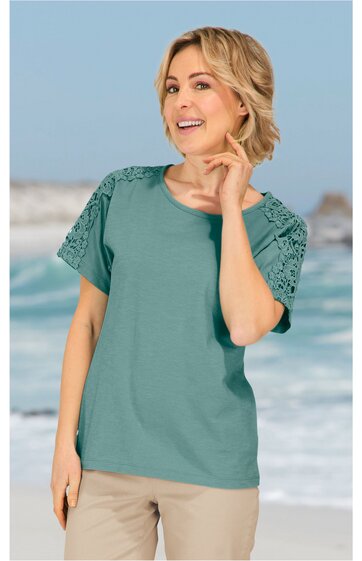 Grünes T-Shirt mit Spitzenärmeln, rundhals, kurzärmelig, gerade geschnitten, getragen von lächelnder stehender Frau mit leicht angewinkeltem rechten Arm