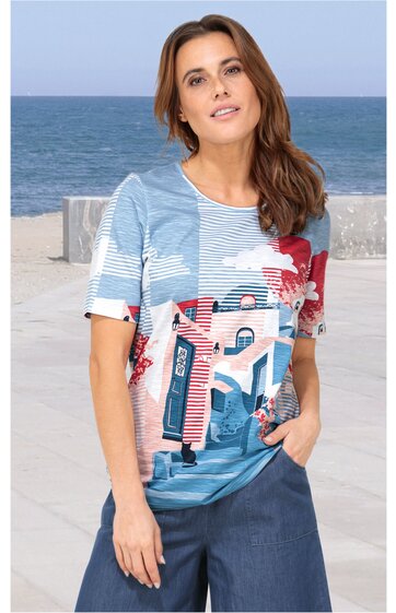 Kurzärmeliges T-Shirt in Hellblau, Weiß und Rot mit grafischem Design aus Zahlen und Linien, Rundhalsausschnitt, gerade geschnittener Saum, getragen von stehender Frau vor Meereshintergrund