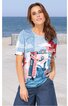 Kurzärmeliges T-Shirt in Hellblau, Weiß und Rot mit grafischem Design aus Zahlen und Linien, Rundhalsausschnitt, gerade geschnittener Saum, getragen von stehender Frau vor Meereshintergrund