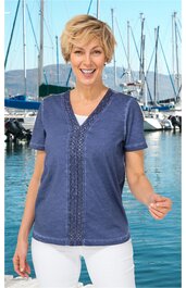 Damenshirt in taubenblau mit kurzem Arm, breitem V-Ausschnitt, durchgehender Spitzenborte in der Mitte, gerade geschnitten, getragen von lächelnder stehender Frau vor Hafenkulisse