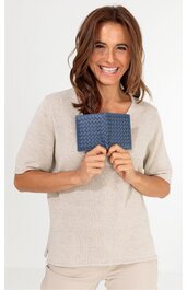 Rechteckige, dunkelblaue Geldbörse mit geprägtem Muster, gehalten von lächelnder Frau mit beige kurzem Armshirt, stehende Position, tragbar als kleines Accessoire