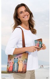 Einkaufstasche mit braunem Schulterriemen, Vorderseite mit buntem Motiv von vier Katzen in verschiedenen Farben sitzend, dazu passende kleine Brieftasche mit gleichem Katzenmotiv, getragen von lächelnder Frau in weißem Dreiviertelarmshirt und beiger 
