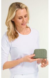 Kompakte Geldbörse in Olivgrün mit gewebter Struktur, rechteckige Form, Reißverschluss rundum, gehalten von Frau mit hellblondem, schulterlangem Haar, weiße Langarmbluse, stehende Pose, kleine Größe