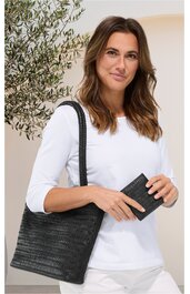 Schwarze Handtasche mit geflochtenem Muster, rechteckig, lange Henkel, gehalten von stehender Frau in weißem Langarmshirt, kombiniert mit schwarzem Portemonnaie in rechter Hand