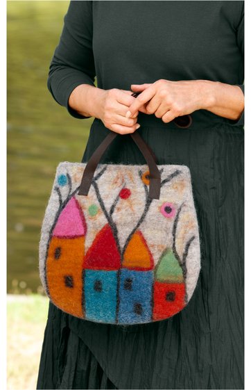 Filztasche in graubraun mit buntem Muster aus stilisierten Häusern in orange, rot, blau und grün, schwarze Tragegriffe, abgerundete Form, gehalten von Person in schwarzem langärmligem Oberteil und schwarzem Rock