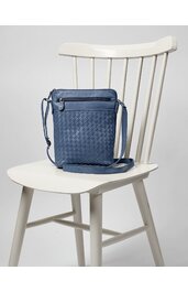 Schultertasche dunkelblau mit Flechtmuster, rechteckige Form, Reißverschlussfach vorne, verstellbarer Schulterriemen, auf weißem Holzstuhl sitzend