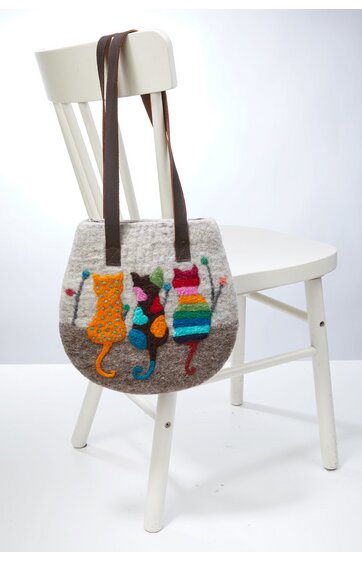 Runde Handtasche in hellem Grau mit bunten applizierten Katzenmotiven in Orange, Schwarz, Grün und Rot, braune lange Trageriemen, an weißem Stuhl hängend