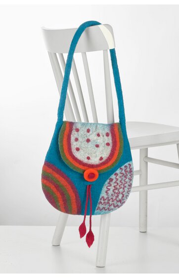 Bunte Schultertasche in Blau mit mehrfarbigem Kreismuster, orangefarbenem Rand, rotem Knopfverschluss, länglichem Trageriemen, hängend an weißem Holzstuhl