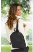 Schwarzer Rucksack mit zwei Reißverschlüssen, glatte Oberfläche, schlichter Look, Rückenansicht, getragen von lachender Frau mit langem braunem Haar und weißem Oberteil, draußen in grüner Umgebung
