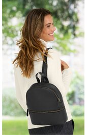 Schwarzer Rucksack mit zwei Reißverschlüssen, glatte Oberfläche, schlichter Look, Rückenansicht, getragen von lachender Frau mit langem braunem Haar und weißem Oberteil, draußen in grüner Umgebung