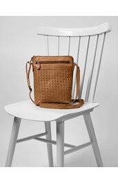 Braune Umhängetasche mit geflochtenem Muster, rechteckig, mit Reißverschlussfach vorne, verstellbarem Schulterriemen, auf weißem Holzstuhl sitzend
