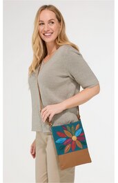 Damenoberteil in hellgrau, kurzärmlig, locker sitzend, V-Ausschnitt, getragen von seitlich stehend lächelnder Frau, kombiniert mit beigefarbener Hose, dazu braun-blaue Umhängetasche mit buntem Blumenmuster vorne