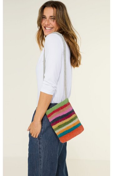 Bunte Umhängetasche mit horizontalen Streifen in Grün, Pink, Rot, Gelb, Blau und Orange, rechteckige Form, getragen von seitlich stehender Frau mit weißem Langarmshirt und blauer Hose