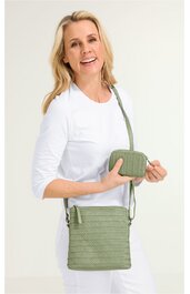 Olivgrüne Umhängetasche mit Flechtmuster, rechteckig, mit Reißverschluss oben, längenverstellbarer Schultergurt, dazu passende kleine Geldbörse, getragen von lächelnder Frau in weißem Oberteil und weißer Hose