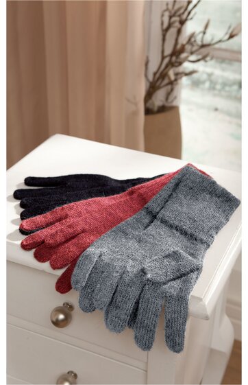 Drei Paar Strickhandschuhe in Dunkelgrau, Bordeauxrot und Hellgrau, fingerförmig, flach liegend auf weißem Nachttisch mit zwei Schubladen, hintergrund unscharf mit Vorhang und Kahlem Zweig in Vase