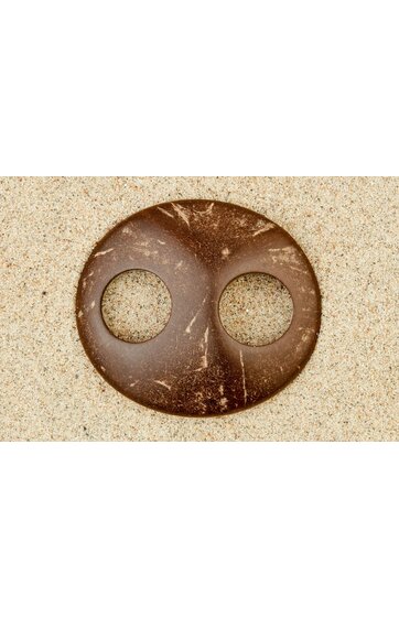 Rundes, braunes Objekt mit zwei kreisrunden Aussparungen, glatte Oberfläche mit leichten Kratzern, liegt auf sandigem Untergrund