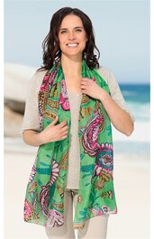 Grüner Damenschal mit buntem Paisley- und Blumenmuster, lang, getragen von lächelnder Frau mit hellbeiger kurzärmeliger Bluse, vor blauem Himmel und Meer