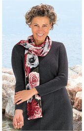Dunkelgraues langärmeliges Kleid ohne Muster, gerade geschnitten, Schalkragen fehlend, getragen von lächelnder Frau mit kurz gelocktem Haar, stehende Pose, mehrfarbiger Schal mit floralem Muster in Rot-, Rosa- und Schwarztönen locker um den Hals gele
